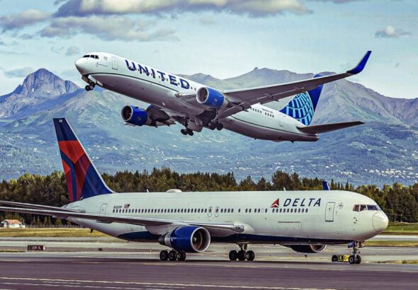 United Airlines jet lifting off the runway as a Delta airplane sits on the ground, with mountains in the background on a clear day.
